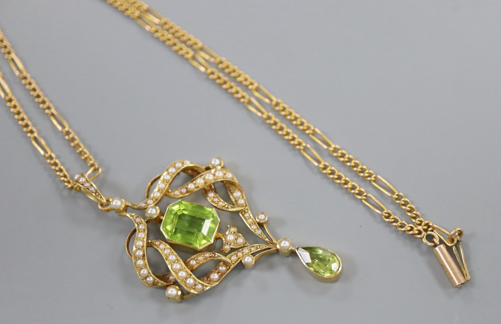An Edwardian gold, seed pearl and two stone peridot set scroll pendant, overall 53mm, gross 7.4 grams, on 9ct chain.